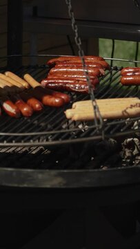 Meat sausages are cooked and browned with fatty smoked crust on large round hanging grill. Massive fatty food harmful to health. Vertical video of kitchen without electricity in nature.
