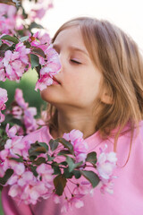 Spring flowering. Portrait of a beautiful little girl 4 years old in a pink blouse in nature against a background of pink flowering apple trees. Childhood. The baby is posing.