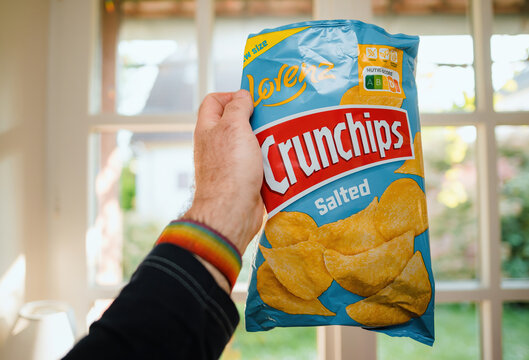 Paris, France - May 2, 2023: A mans hand holds a bag of Lorenz Salted Crunchips, ready to enjoy their salty snack goodness kitchen background