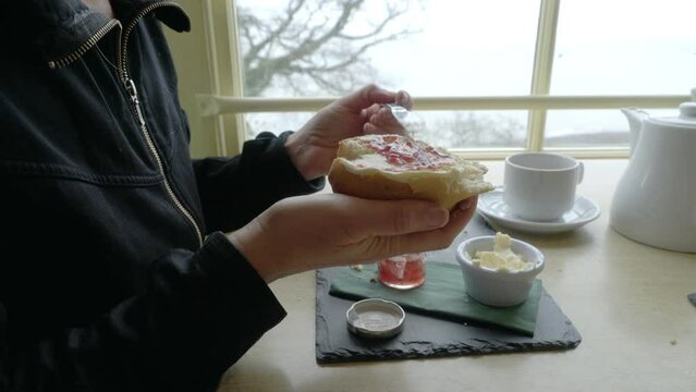 Woman putting jam on cream tea scone in restaurant