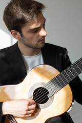 Portrait of a young boy playing the guitar. He is wearing a black suit