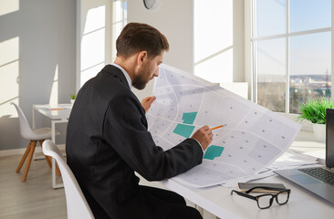 Businessman analyzing cadastral map while sitting at desk in office. Cadastral engineer,...