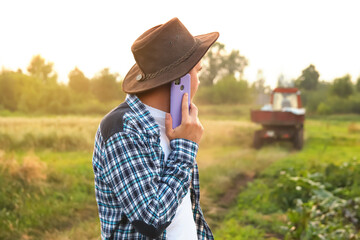 Farmer talking on the purple phone on the tractor background. Amidst the vast expanse of a field, a...