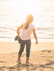 girl at the beach on a sunny afternoon using binoculars, walking and kicking the sand, Girl Looking at the beach through binoculars on a sunny afternoon, backlit, walking and smiling, kicking up the s