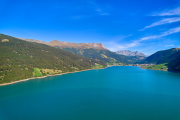 Fototapeta premium Aerial view of lake (Reschensee). Large reservoir surrounded by mountains at sunny noon. Recreation area for tourists and sportsmen. Italy, Vinschgau, Reschen.