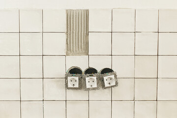 Stylish white tiles and electricity socket close up on wall. Modern square tile installation on adhesive and electric box. Kitchen or bathroom renovation, home improvement