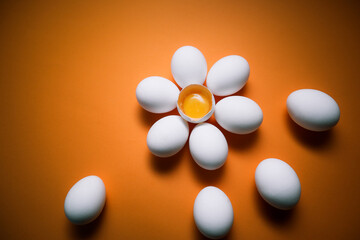 Flower shaped raw egg on orange background. Few white eggs, whole and broken egg half with a yolk isolated on a white background