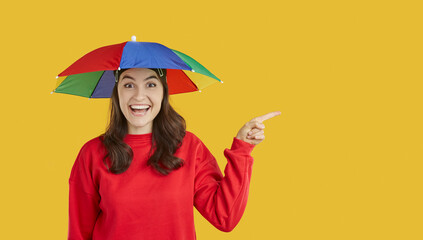 Funny woman with head umbrella pointing finger at copy space presenting seasonal discount promo offer. Joyfully surprised girl pointing with finger sideways at space for text on orange background.