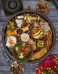 Cheese and snacks board on wooden table, consisiting of crackers, nuts, salad. cheeses, olives, pickles