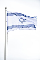 Fototapeta premium Israel state flag blown by the wind on a pole with clear sky on background