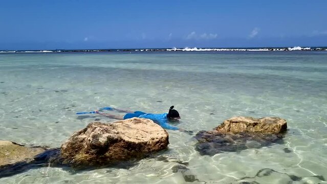 Man in blue snorkeling on a Caribbean shore swimming andfilming fishes with small underwater camera. High quality FullHD footage