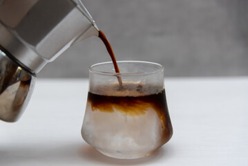 Coffee is poured from a moka pot into a glass with ice.