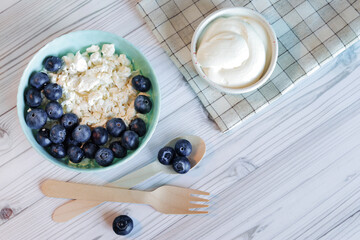 Healthy breakfast. Cottage cheese with blueberries, top view. Healthy keto breakfast concept, fresh berries and cottage cheese with sour cream. Plate with healthy breakfast and wooden spoon and fork
