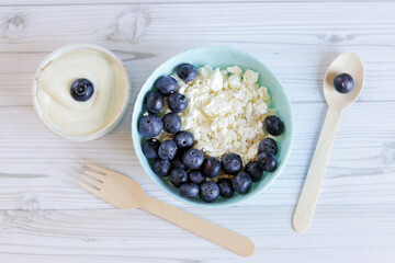 Cottage cheese with blueberry, fresh berries, keto healthy breakfast concept, top view. Plate with healthy breakfast and wooden spoon and fork