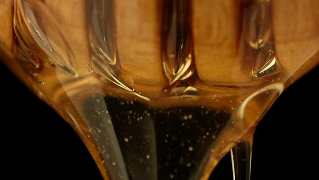 Honey dripping, pouring from wooden dipper close up on black background. Healthy organic honey