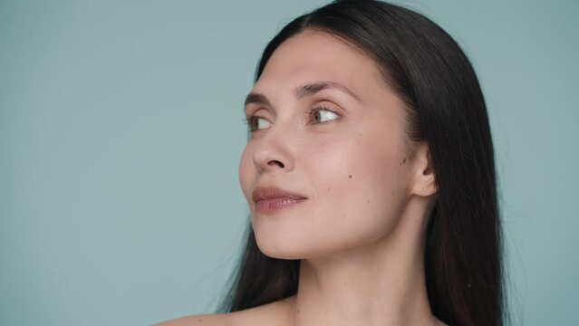 The woman demonstrates the perfect clean and fresh skin of the face, turning her head from one side to the other. Close up face of a young woman in the studio on a blue background.