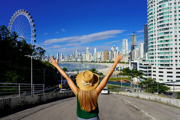 Girl with raised arms on Balneario Camboriu skyline with Ferris Wheel, Santa Catarina, Brazil