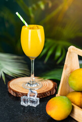 Glass of mango juice smoothie with ice cubes and mango fruit on the background