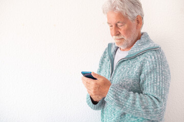 Serious senior white-haired man using phone standing on white background. Old bearded people holding smartphone in hand typing message