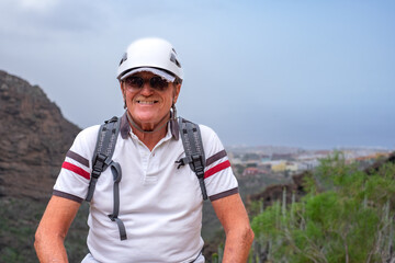 Smiling senior hiker man wearing helmet walking on mountain enjoying a trekking day - Carefree climbing tourist in holidays and healthy lifestyle - Freedom, health, sport concept