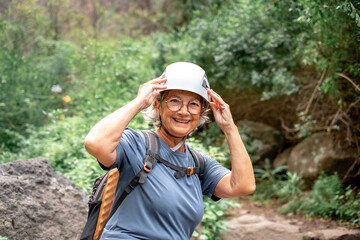Naklejka na ściany i meble Smiling senior hiker woman wearing helmet in a trekking mountain day - Carefree climbing tourist in holidays and healthy lifestyle - Active grandmother enjoying freedom and nature