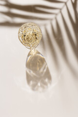 White wine in crystal transparent fashion glass with palm leaf shadow at sunlight, beige background and beautiful light, creative summer alcohol drink minimal concept, copyspace, top view