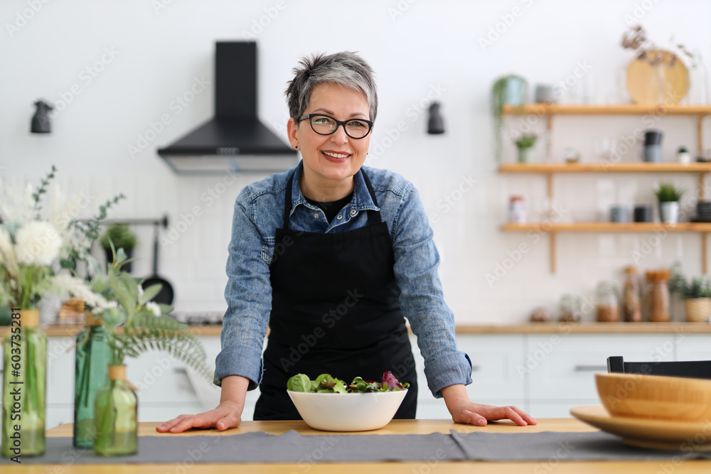 Wall mural Woman in the kitchen with a plate of salad on the table, smiling.