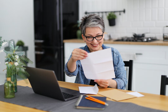 Happy Mature Woman In Glasses Opens Mail Documentation At The Table.