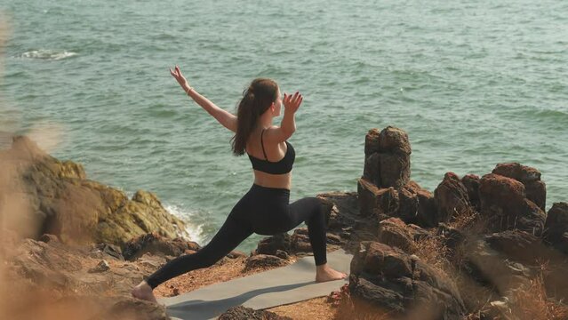 Girl is doing Ashva Sanchalanasana on a seaside rocky shore