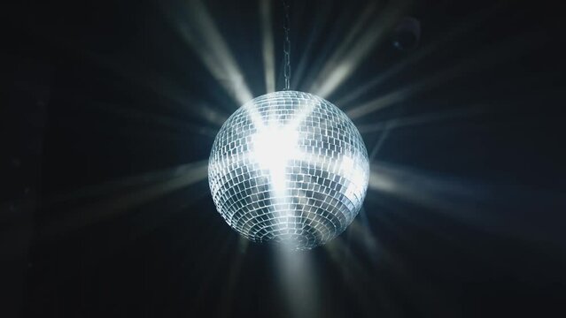 Disco Ball with Reflected Moving Rays Rotating. Mirror disco ball in white light. Isolated disco ball on black background. Close-up. Mirror ball spinning indoors. Performance. The reflection of lights