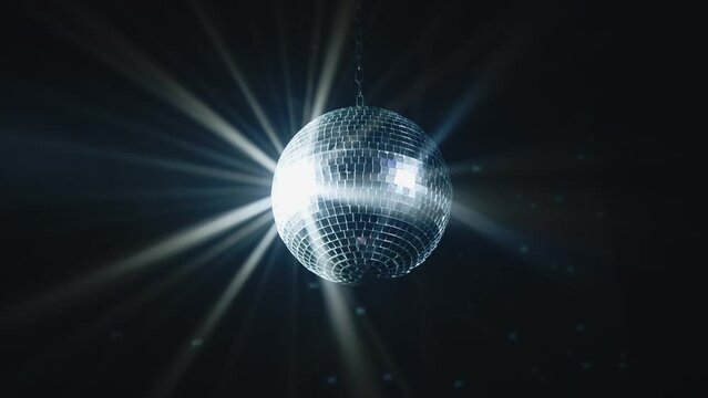 Disco Ball with Reflected Moving Rays Rotating. Mirror disco ball in white light. Isolated disco ball on black background. Close-up. Mirror ball spinning indoors. Performance. The reflection of lights