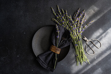 High angle of summer table setting with lavender flowers on black concrete dark background between a napkin on plate and scissors