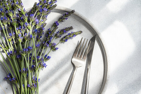High angle of summer table setting with lavender flowers on a plate with fork and knife against grey background