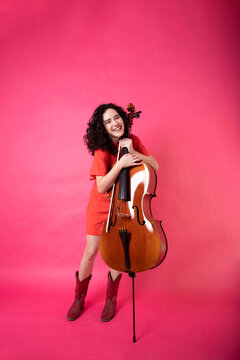 Cheerful young woman with cello over pink background