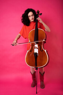 Young woman playing cello over pink background