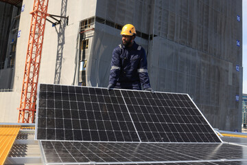 Male technicians carrying photovoltaic solar module on roof top of factory. Engineers in helmets...