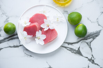 Fresh uncooked tuna steaks with flowers and limes on a white marble background, horizontal shot, top view