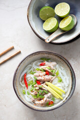 Bowl of Pho Ga or vietnamese traditional chicken noodle soup, vertical shot on a light-beige stone background, elevated view