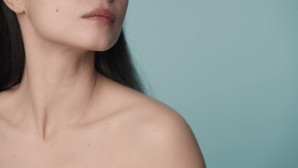 The seminude woman runs her well groomed hand over her chin and down to her neck. Close up of the perfect chin and slender neck of a woman on a blue background. Skin care, body care, cosmetology.