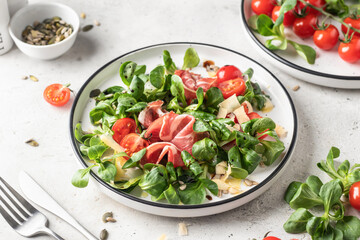 Fresh Green salad with ham or prosciutto, corn salad leaves, tomatoes and cheese. Healthy diet lunch on white marble background