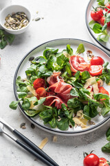 Green salad with ham or prosciutto, corn salad leaves, tomatoes and cheese. Healthy diet lunch on white marble background