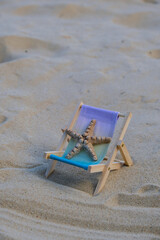 Fototapeta premium Sunny holidays on the beach with sand beach accessories with sea shells and sea star. Sun lounger stand sea Ocean background. Wooden beach chairs. Summer holiday vacation concept. 
