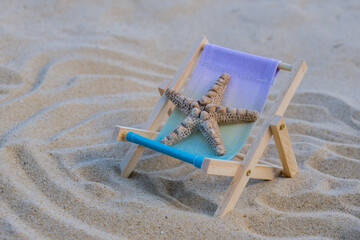 Fototapeta na wymiar Sunny holidays on the beach with sand beach accessories with sea shells and sea star. Sun lounger stand sea Ocean background. Wooden beach chairs. Summer holiday vacation concept. 