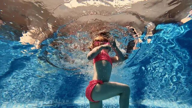 Positive, cute, little baby girl, toddler in pink swimsuit and goggles diving, swimming underwater in swimming pool. Water sports. Concept of sport, healthy and active lifestyle, childhood, fun