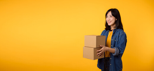 Portrait asian young woman wearing yellow t-shirt and denim shirt holding parcel box isolated on...