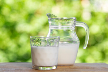 Glass cup and jug full of fresh cow's milk on wooden table with rustic blurred natural landscape background. Fresh cow's milk in a glass in nature ready to drink. Cow's milk concept