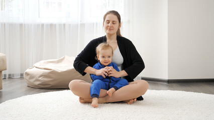 Happy smiling young mother teaching her little baby son doing yoga asana while practising yoga. Family healthcare, active lifestyle, parenting and child development