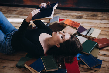 A relaxed woman underlie and reads in a room full of books.