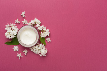 Obraz na płótnie Canvas Jar with cream and flowers on color background, top view