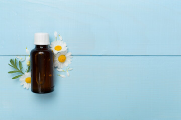 Bottle with chamomile essential oil and flowers on wooden background, top view